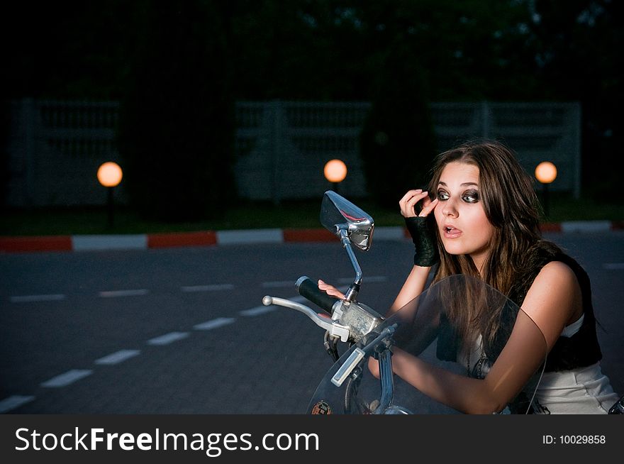 Glam biker model fixing up her makeup in the motorcycle mirror. Glam biker model fixing up her makeup in the motorcycle mirror