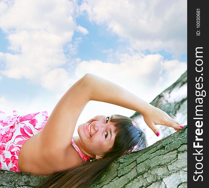 Young attractive girl laying on tree on sky background