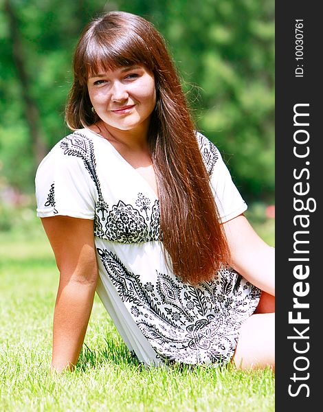 Young attractive girl sitting on green grass in park