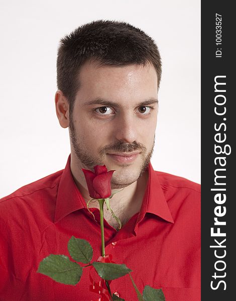 Young, handsome man in red shirt, holding a beautiful red rose in front of his mouth. Young, handsome man in red shirt, holding a beautiful red rose in front of his mouth