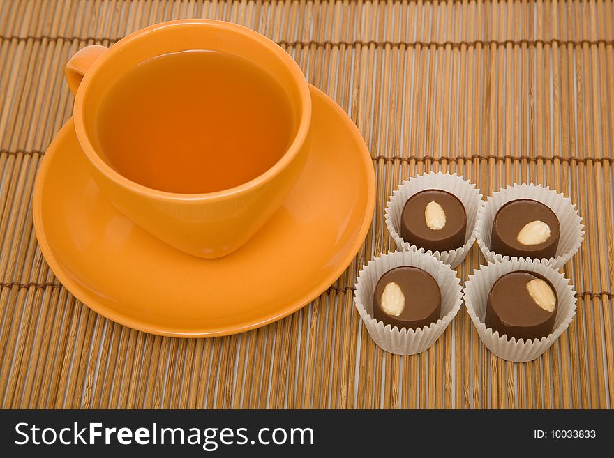 Cup of tea and four chocolate sweets on a bamboo mat