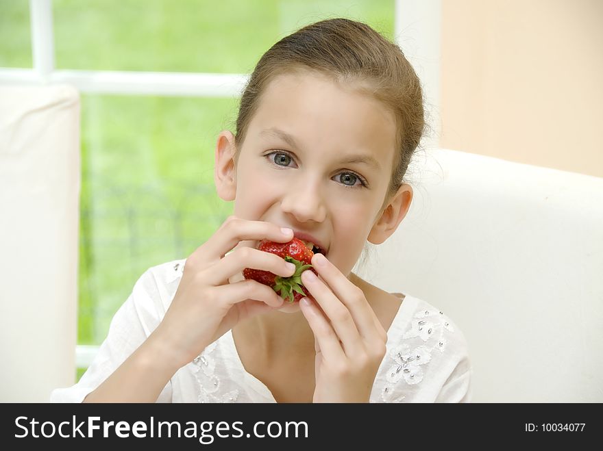 Pretty girl sitting on white chair,taking big fresh strawberry to close to mouth