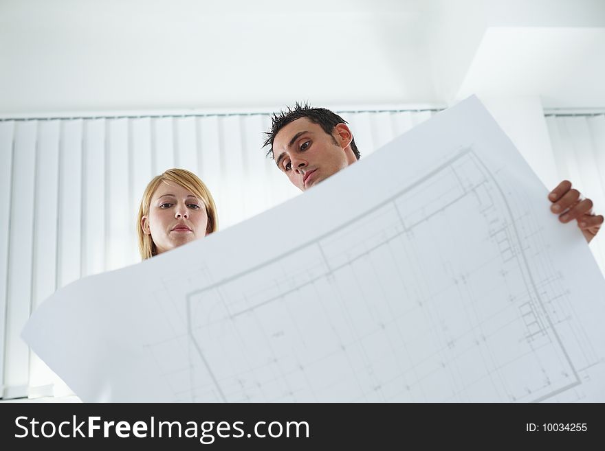 Two architects examining blueprint indoors. Low angle view. Copy space