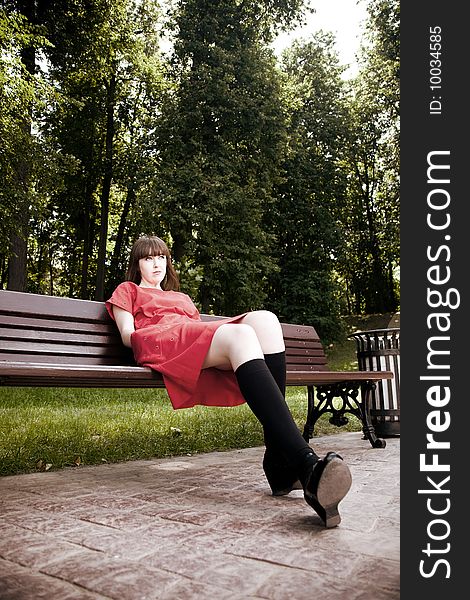 Beauty Woman Sitting On A Park Bench Under The Sunlight