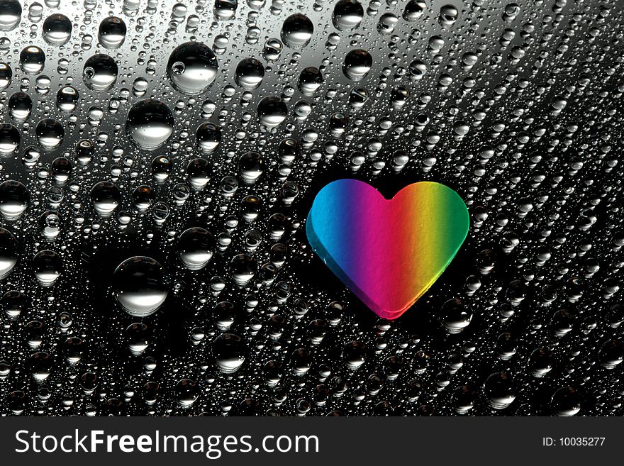 Colorful paper heart with water drops against black background