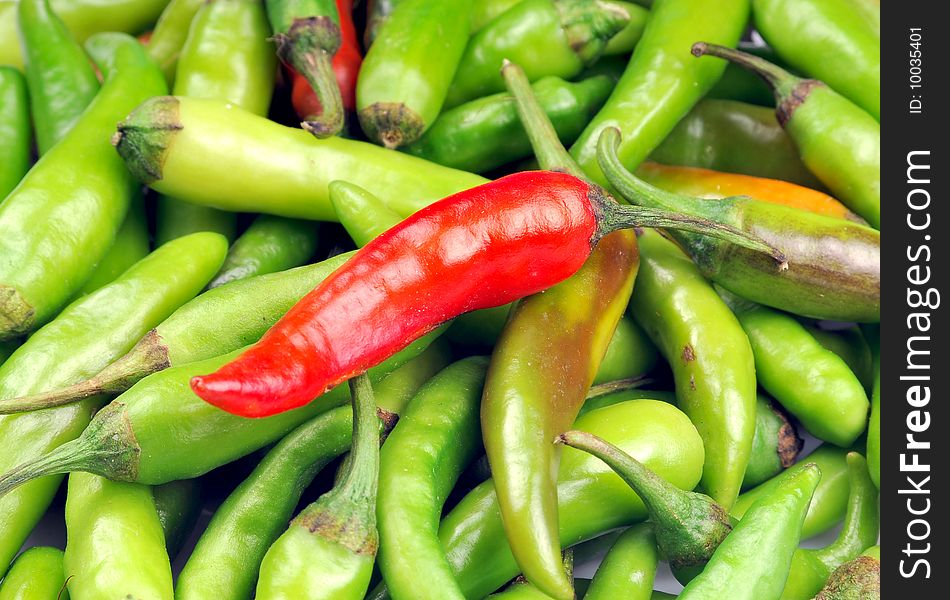 Heap of green chillies with red one on top.