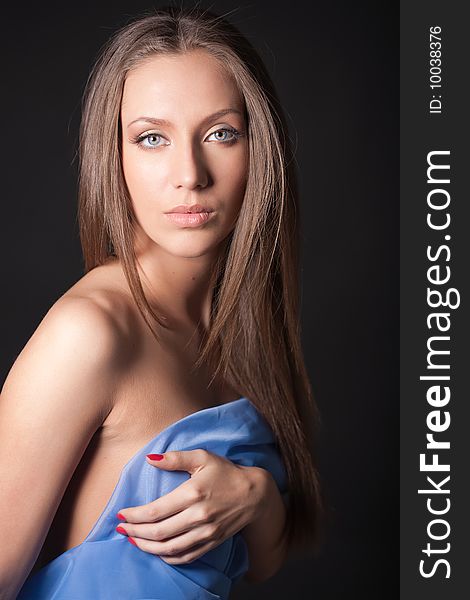 Portrait of attractive girl covering your body in blue silk. Over black. Portrait of attractive girl covering your body in blue silk. Over black