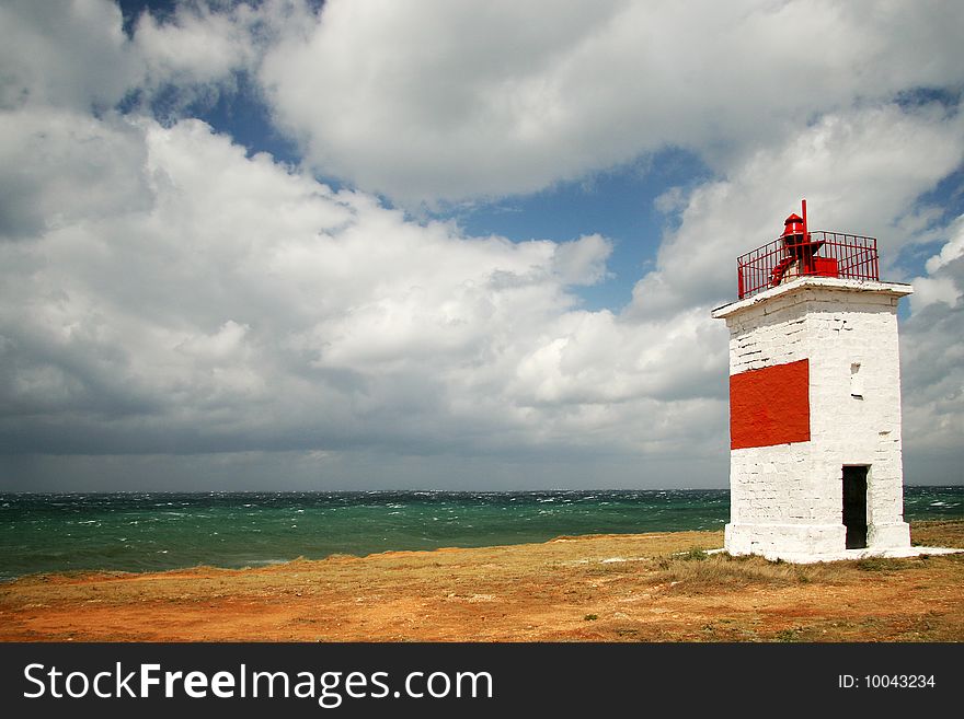 Beacon on seacoast with a yellow grass and white clouds in the sky