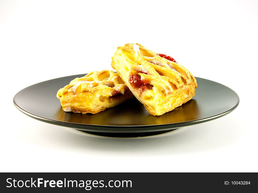 Raspberry and custard danish on a black plate on a white background. Raspberry and custard danish on a black plate on a white background