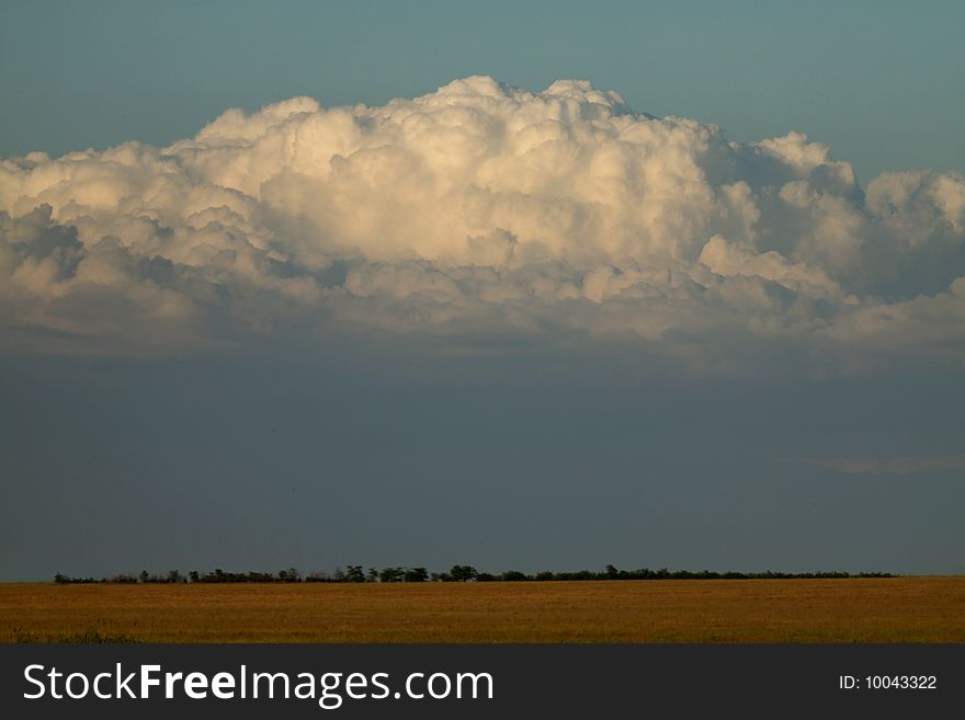 Clouds in the form of mountain in the evening over a dark yellow field. Clouds in the form of mountain in the evening over a dark yellow field