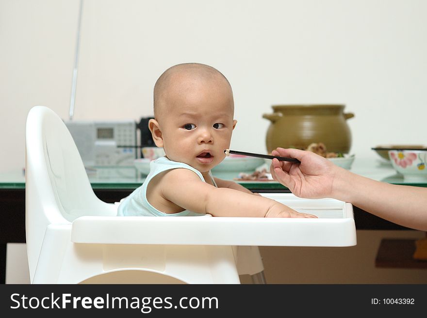 A Chinese mother is feeding baby in highchair.