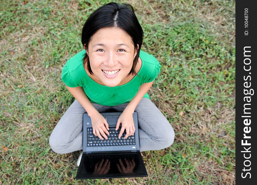 An Asian girl relaxes outdoors with her laptop. An Asian girl relaxes outdoors with her laptop.