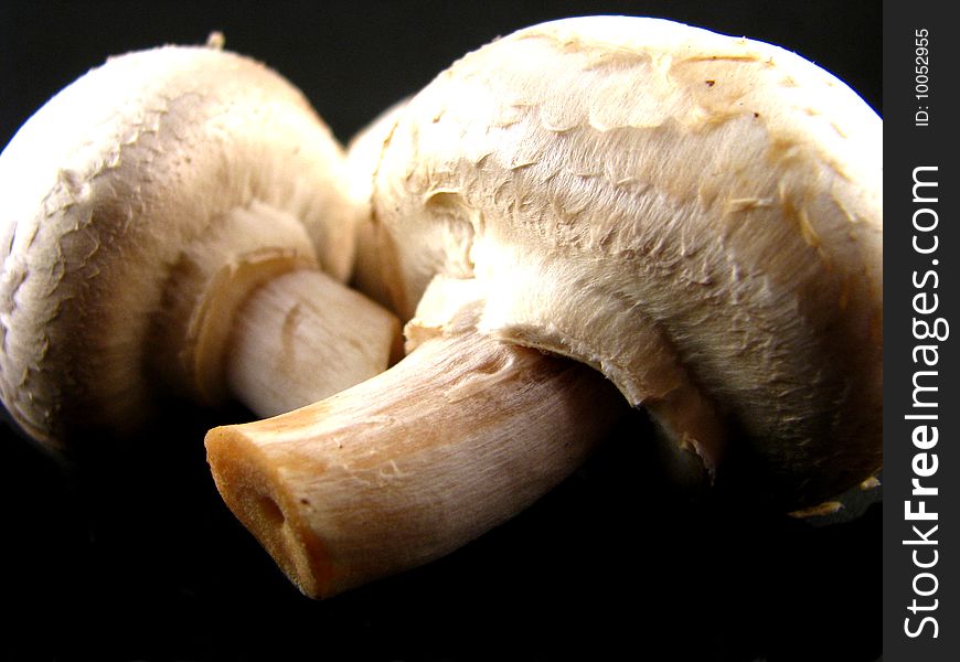 Two fresh, raw white button mushrooms on a black background