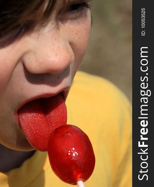 Close up of a young boy enjoying a red lollipop on a summer day