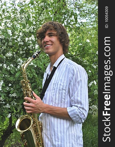 Beautiful boy with saxophone on background of flowering apple-tree. Beautiful boy with saxophone on background of flowering apple-tree