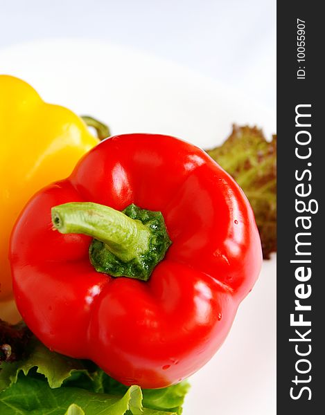 Red sweet bell pepper on green lettuce leaves, white blur background, closeup, vertical