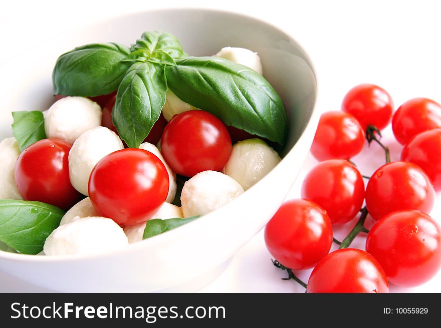 Mozzarella boconccini cheese balls with cherry tomatoes and green fresh basil in a salad bowl on white blur background. Mozzarella boconccini cheese balls with cherry tomatoes and green fresh basil in a salad bowl on white blur background