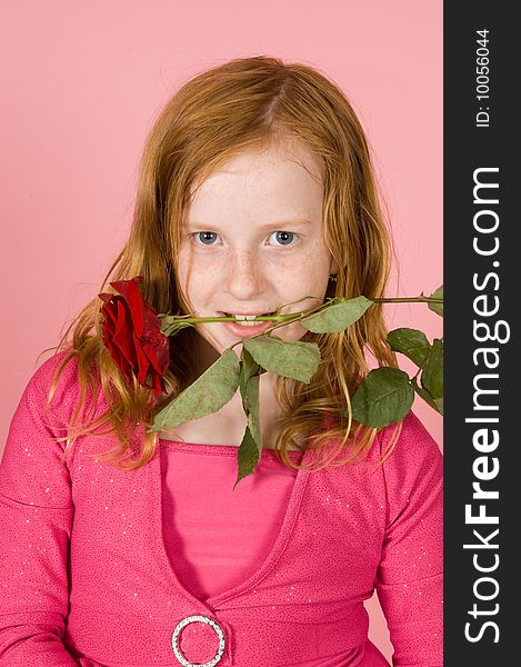 Young girl is holding a red rose between her teeth on pink