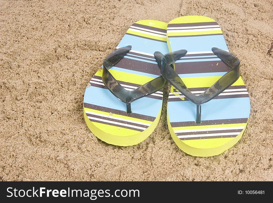 Green colored summer slippers lying on sand