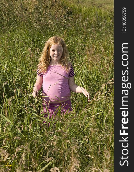 Little girl in pink clothes between high grass meadow