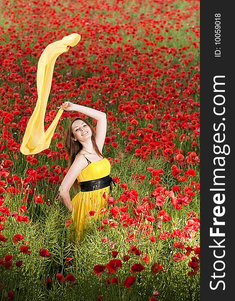 Attractive smiling girl with yellow scarf in the poppy field