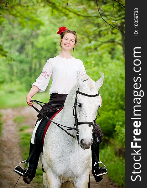 Smiling girl riding white horse in the forest