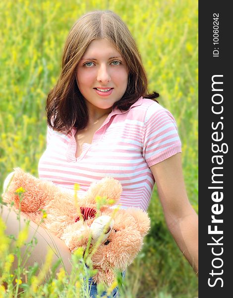 The girl sitting on a summer meadow with a toy bear cub. The girl sitting on a summer meadow with a toy bear cub
