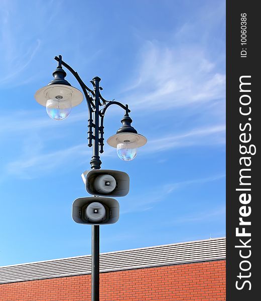 Two loud-speakers on retro lamppost with the red brick wall and blue sky in the background. Two loud-speakers on retro lamppost with the red brick wall and blue sky in the background.