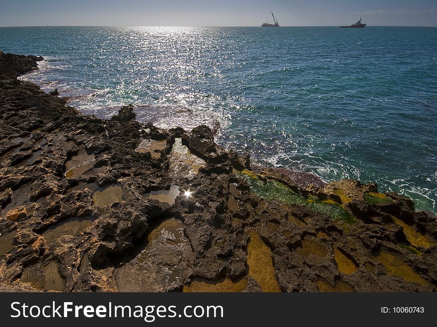 Seashore with colour rocks in foreground and nice blue water, ships on horizon