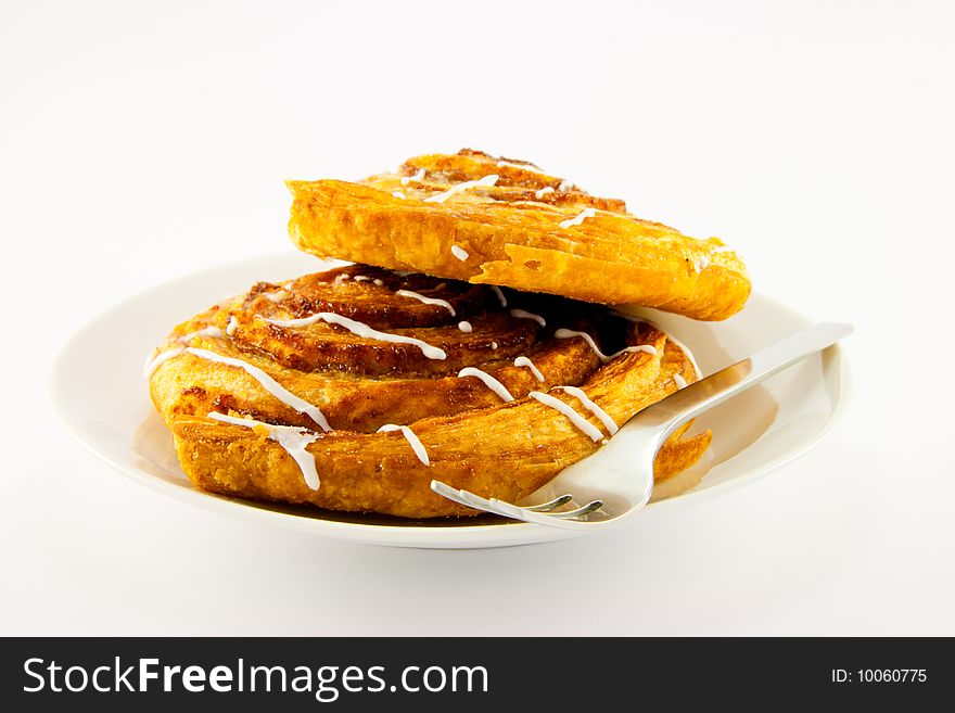 Two cinnamon buns on a plate with a fork with a clipping path on a white background. Two cinnamon buns on a plate with a fork with a clipping path on a white background