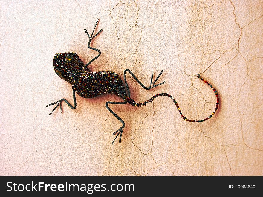 A beaded handmade lizard sitting on a wall in the sun. A beaded handmade lizard sitting on a wall in the sun