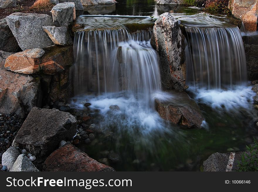 Stream waterfall flows over rocks and mists as it hits the bottom.