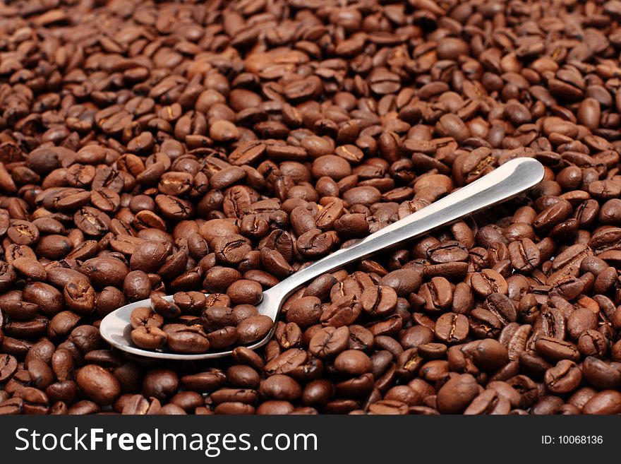 Coffee beans on a spoon which is lying on more coffee beans. Coffee beans on a spoon which is lying on more coffee beans