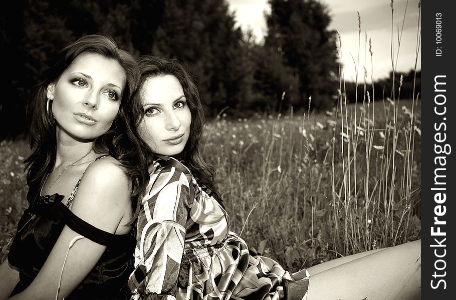 Two sensual girls sitting closely in the grass somewhere outdoors. Two sensual girls sitting closely in the grass somewhere outdoors