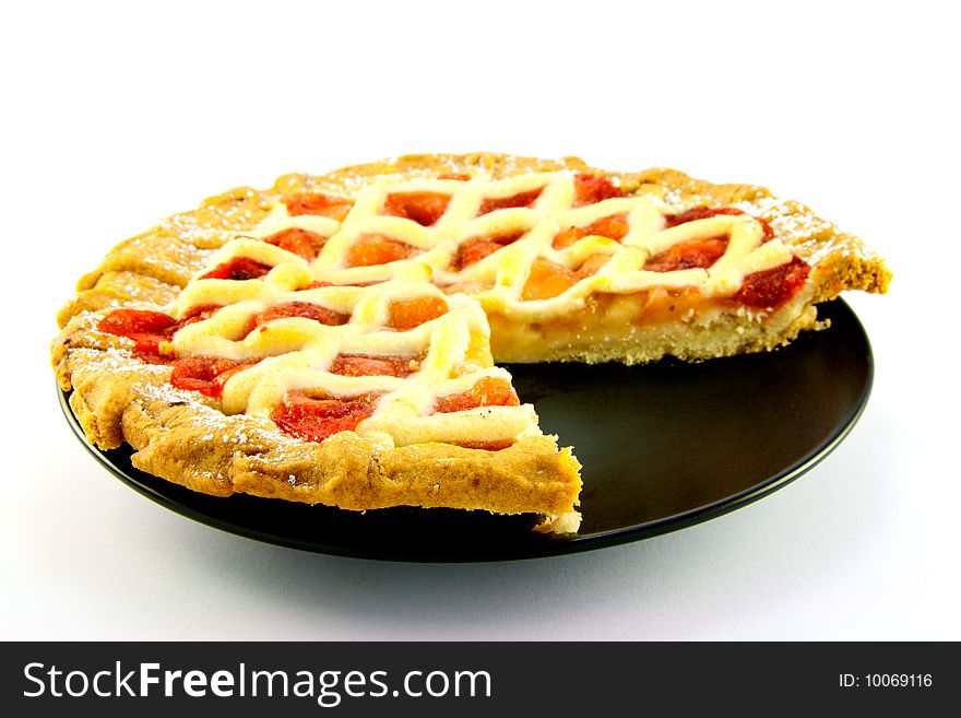 Whole apple and strawberry pie on a black plate with a slice missing on a white background. Whole apple and strawberry pie on a black plate with a slice missing on a white background
