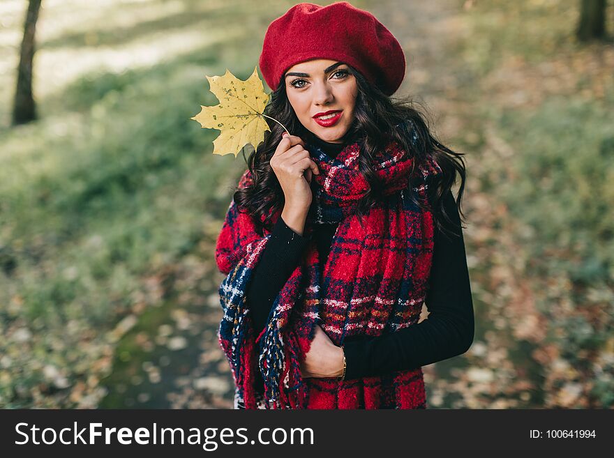 A happy and beautiful woman in a red scarf and hat walks in the park in the autumn by the river. A happy and beautiful woman in a red scarf and hat walks in the park in the autumn by the river.