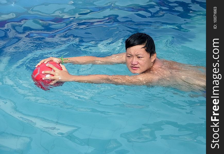 A young man swimming in the pool fetching the ball. A young man swimming in the pool fetching the ball.