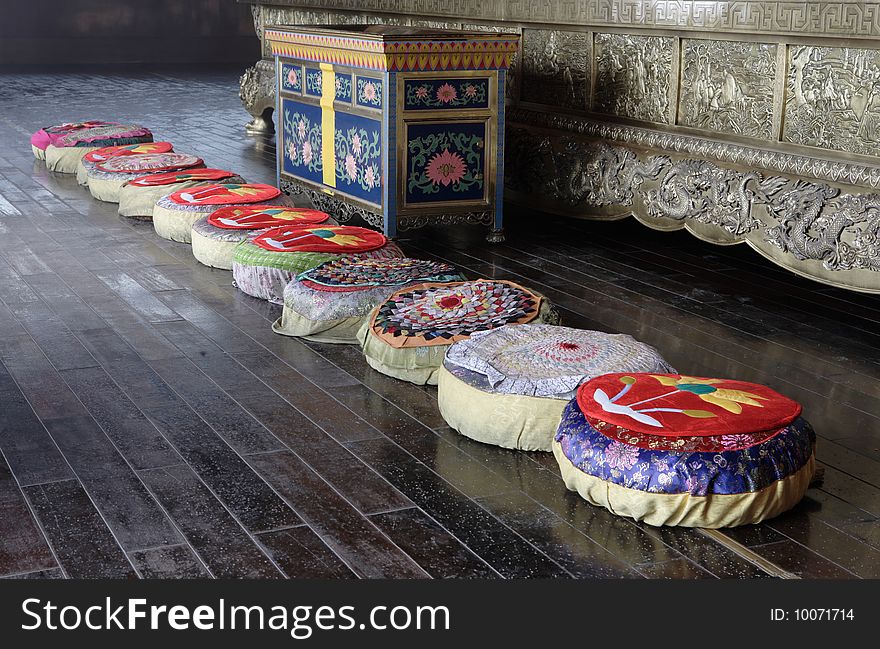 Interior of buddhist temple in China, Emeishan. Diagonal row of pillows for prayers and wooden cub. Dragon ornaments in the background