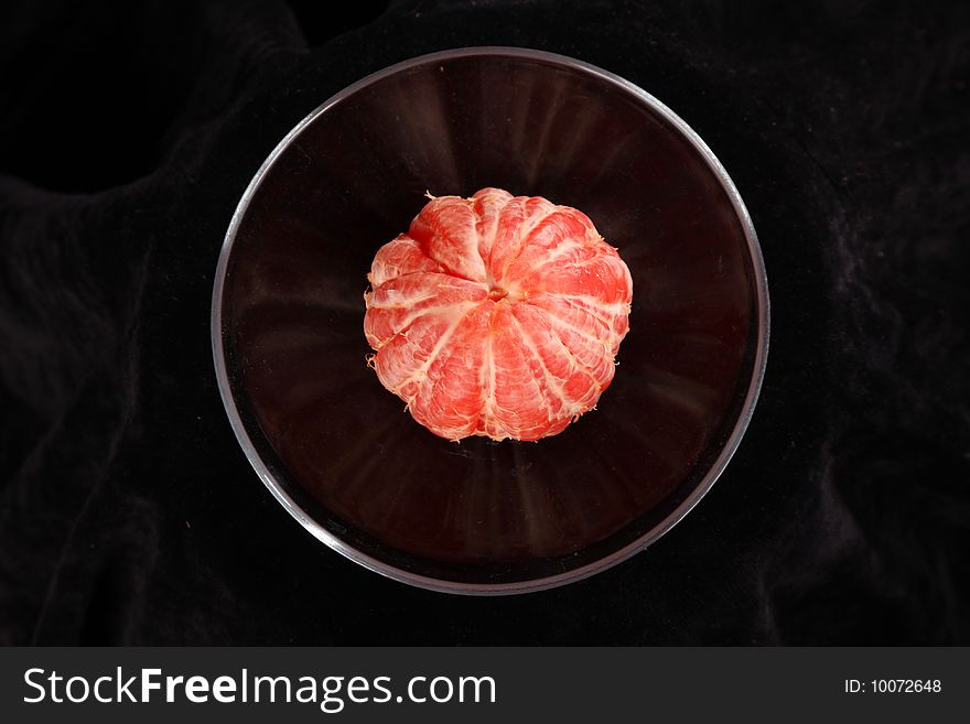 Grapefruit in the transparent plate against the black background, it is taken perpendicularly to the floor