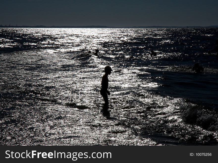 Young boy walking in the shallow sea near the shore line. Young boy walking in the shallow sea near the shore line.