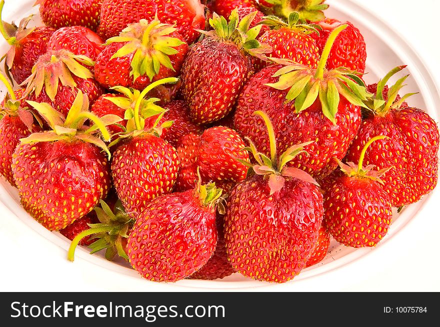 Juicy large strawberry with yellow sunflower seeds on a white plate