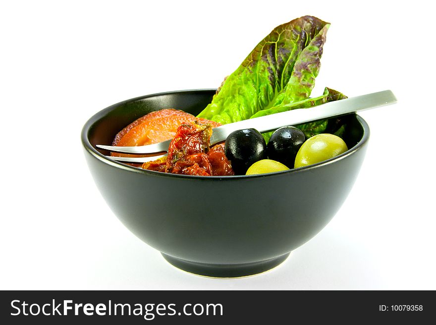 Black bowl with tomatoes, lettace and green and black olives and a small fork on a white background. Black bowl with tomatoes, lettace and green and black olives and a small fork on a white background