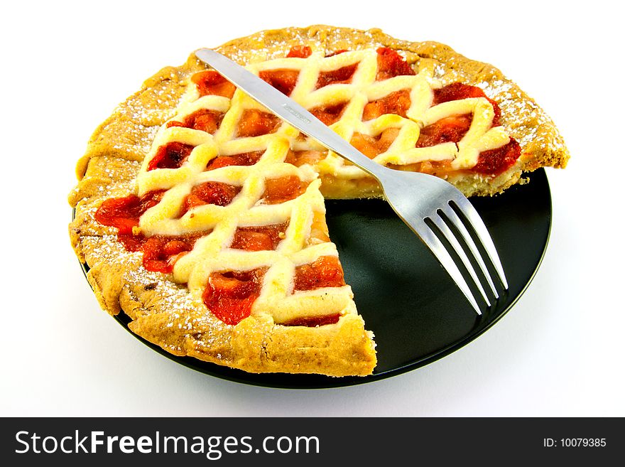 Whole apple and strawberry pie with a small fork on a black plate with a slice missing on a white background. Whole apple and strawberry pie with a small fork on a black plate with a slice missing on a white background