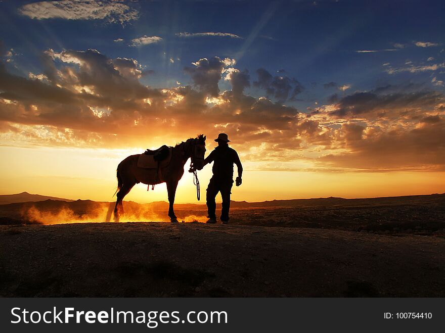 A cowboy stending with his horse and horse is making dust with its feet. A cowboy stending with his horse and horse is making dust with its feet