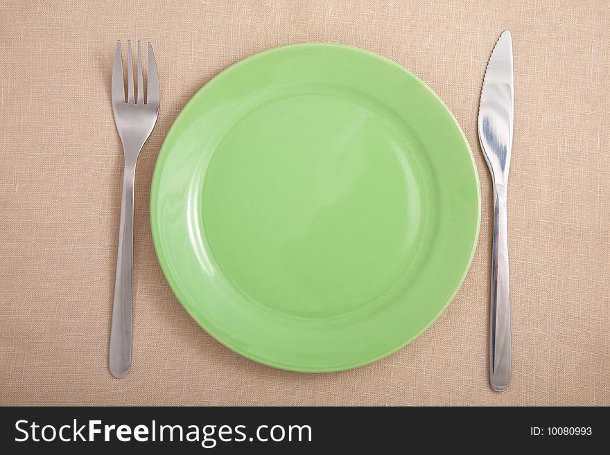 Fork and knife near round green plate. Fork and knife near round green plate