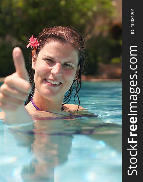 Young woman in a beautiful pool with palms in the background. She is showing a thumbs up sign. Young woman in a beautiful pool with palms in the background. She is showing a thumbs up sign.