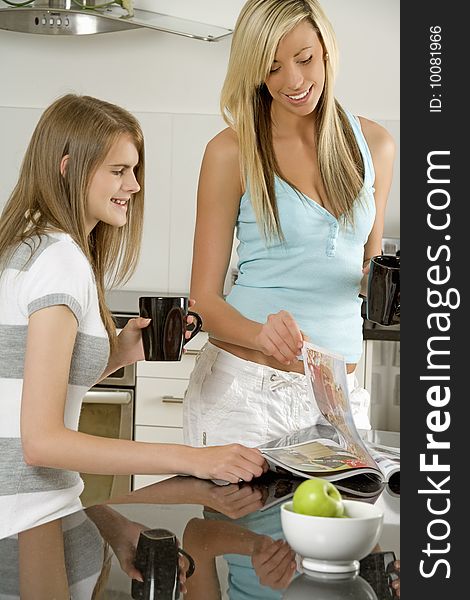 Two female models reading and relaxing in kitchen setting. Two female models reading and relaxing in kitchen setting