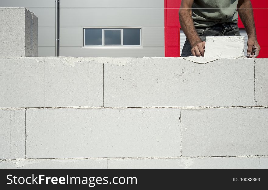 The worker builds the wall using big white bricks. The worker builds the wall using big white bricks