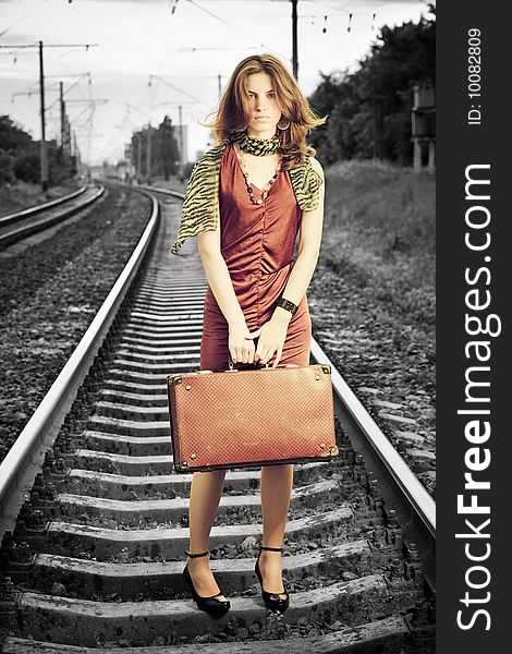 Young beautiful woman with retro suitcase standing on a railway and looking on camera. Emotional retro concept. Young beautiful woman with retro suitcase standing on a railway and looking on camera. Emotional retro concept