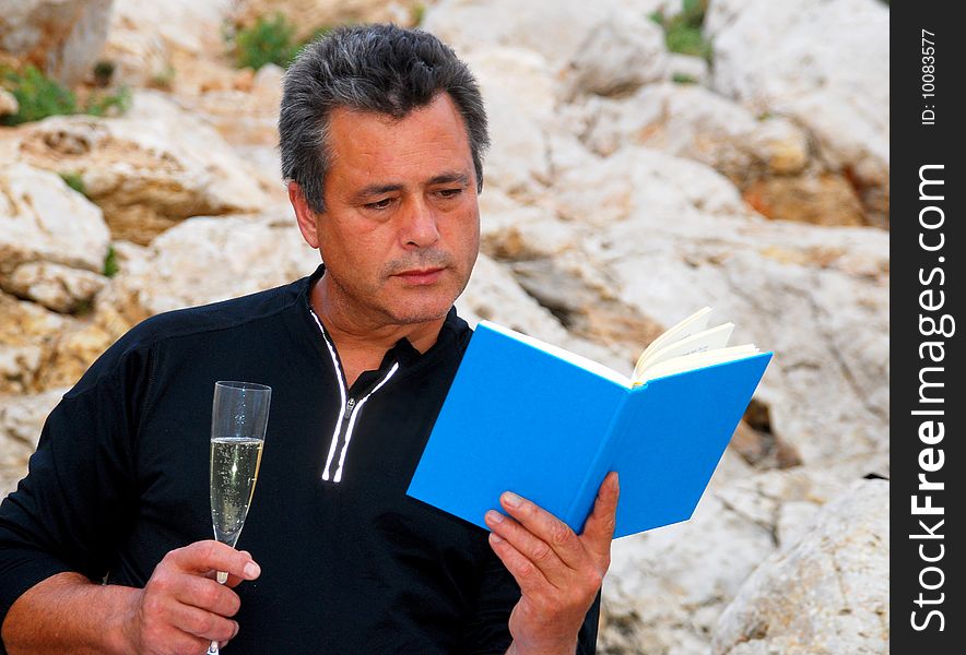 Man with a glass of champagne sitting outdoors reading a book. Man with a glass of champagne sitting outdoors reading a book